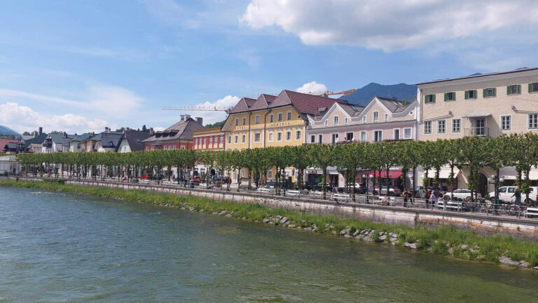 Blick über einen Fluss auf die historische Uferpromenade von Bad Ischl mit farbenfrohen Gebäuden